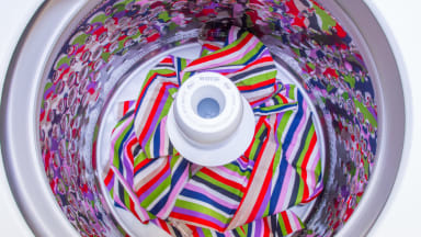 An overhead view of a top-load washer with agitator which is filled with striped sheets.