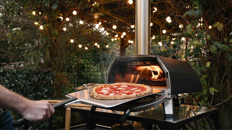 A person takes a cooked pizza out of the Ooni Karu 16 oven.