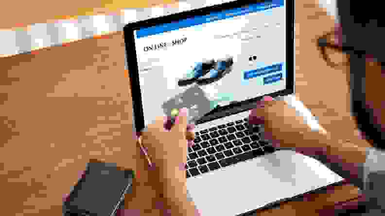 Man holding credit card in front of laptop, typing in card number for an online purchase.