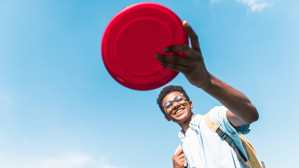 A child flings a red frisbee outside.