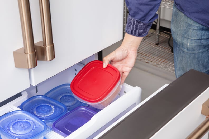 A person puts plastic containers in a freezer drawer