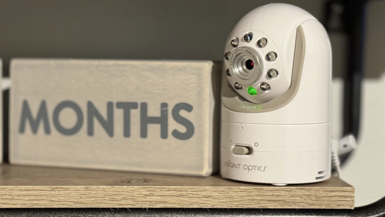 The Infant Optics DXR-8 PRO baby monitor sitting on wooden shelf next to decorative wooden block.