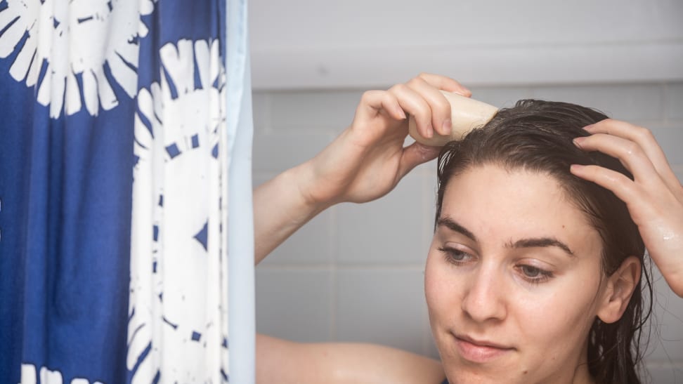 A closeup on a person holding the HiBar shampoo bar up their wet hair as they take a shower.