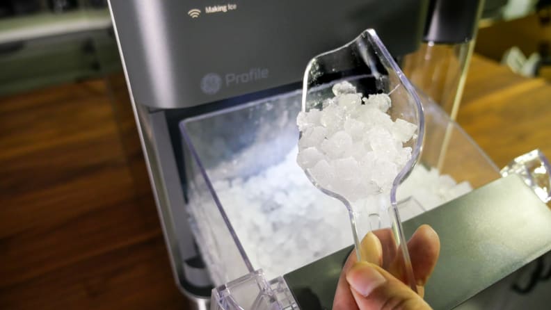 Mão segurando uma colher cheia de pepitas de gelo sobre o GE Profile Opal 2.0
