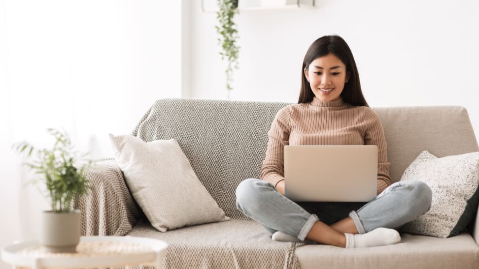 Person on couch smiling while working on laptop at home.