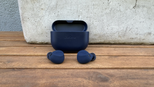 The Jabra Elite 8 Active in navy blue sitting in front of their open case on a wooden table with a stone flower tray behind them.