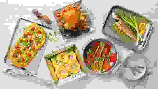 Cooked chicken, fish, pizza and vegetables sit on countertop in All-Clad bakeware dishes