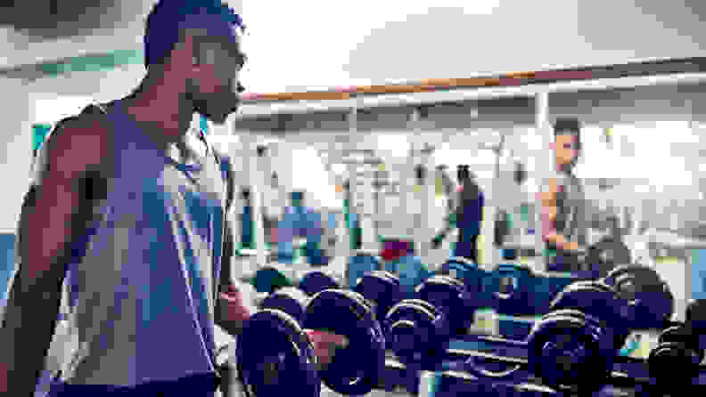 Cropped shot of a handsome young athletic man watching himself in the mirror while working out with dumbbells in the gym