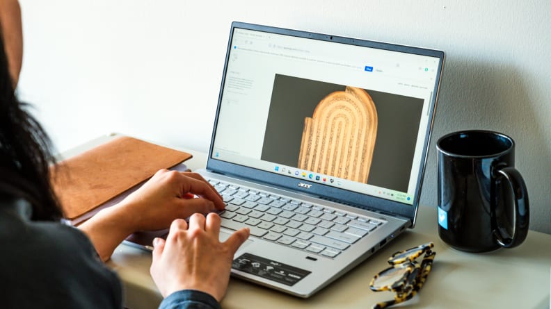 A person holds their fingers over a laptop's keyboard and trackpad while working on a project.