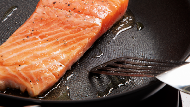 A piece of salmon cooking on a Circulon pan.