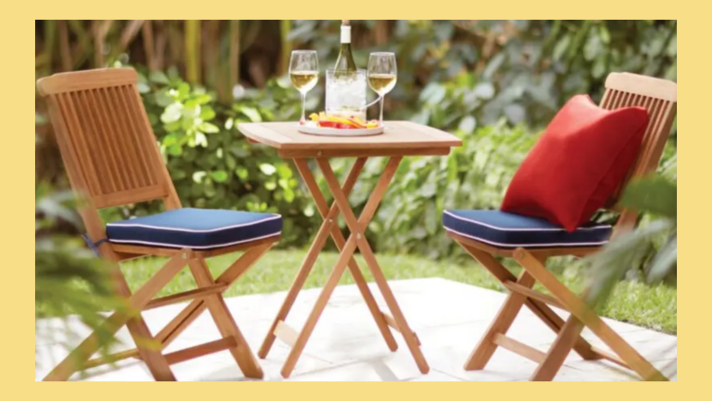 Wooden bistro set with matching blue cushions and one red pillow on a patio