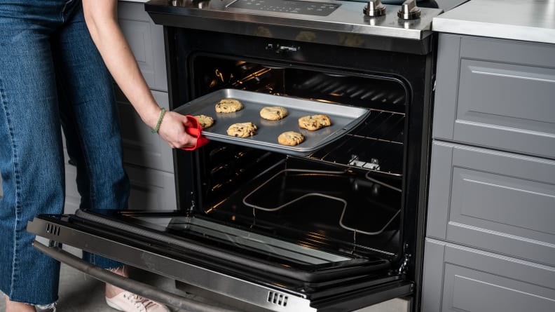 A person removes a tray of cookies from the oven using a red oven mitt.