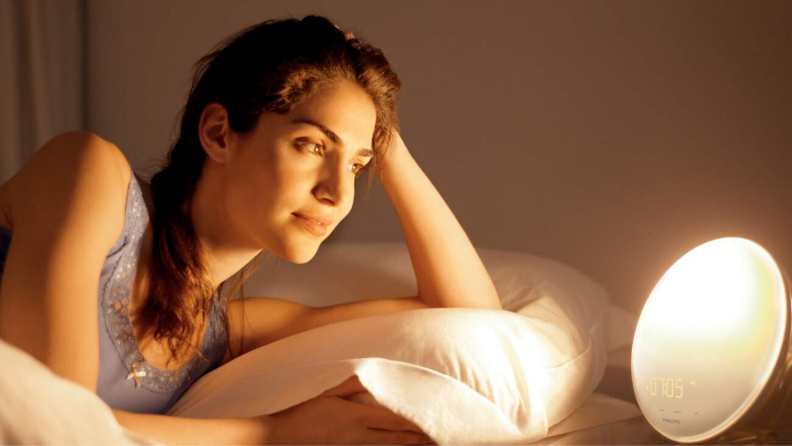 A woman looking at the Philips Wake-Up Light alarm clock on her nightstand