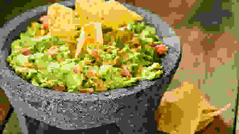A high angle close up of creamy guacamole in a Mexican molcajete and crunchy corn chips. Shot on an old wooden outdoors table