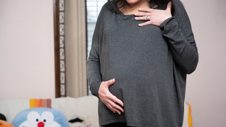 A pregnant woman wears a gray long-sleeved shirt.