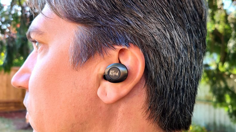 The black enameled Klipsch T5 II True Wireless ANC earbud sits in the ear of a man with salt and pepper brown hair.