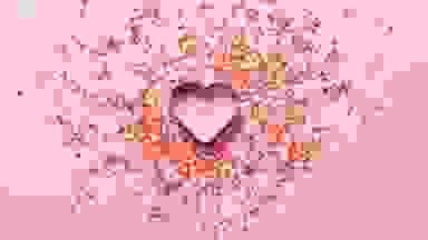 A heart cookie cutter on a pink background with sprinkles