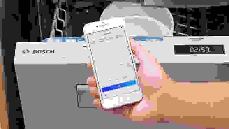 A person holding a phone showing the quadrants in the Home Connect app in front of a Bosch dishwasher.