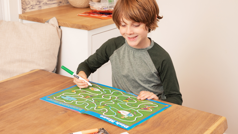 A child sitting at a table doing a maze in the Highlights magazine.