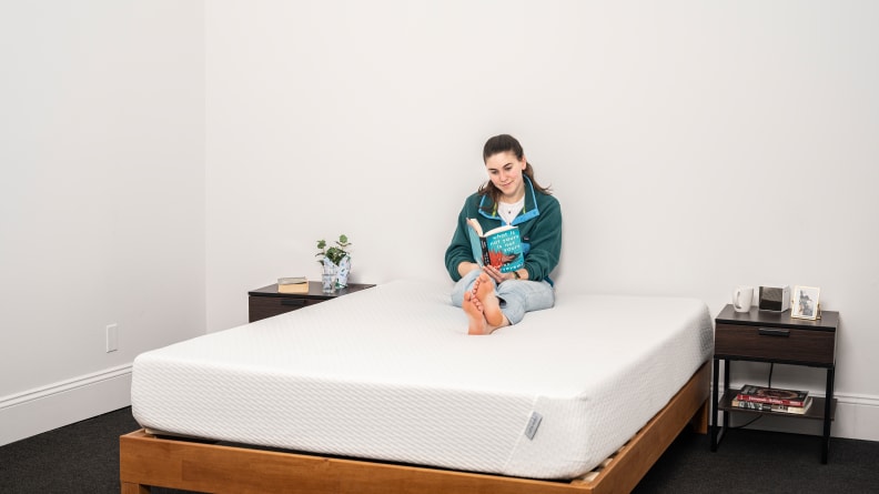 a woman sits and reads on the Tuft & Needle Original mattress