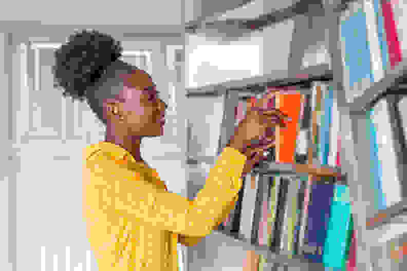 女人从图书馆书架上拿书。年轻的图书管理员正在找书，从图书馆的书架上拿了一本书。