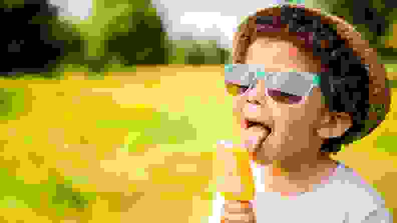 Boy in sunglasses and hat eating popsicle outdoors