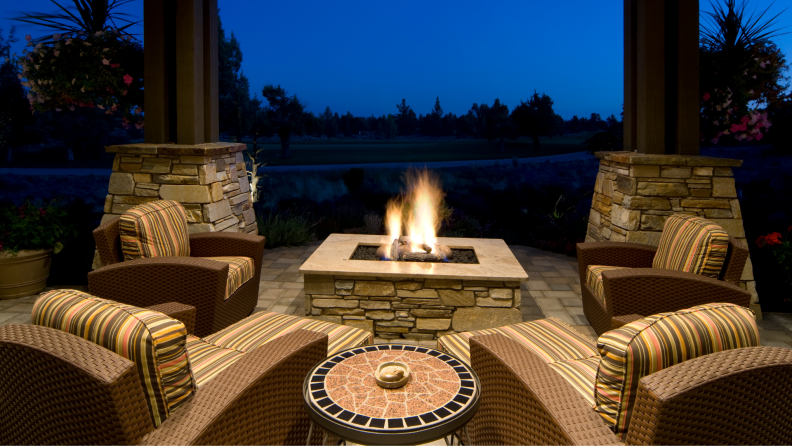 Fire pit burning on patio surrounded by patio furniture at nighttime