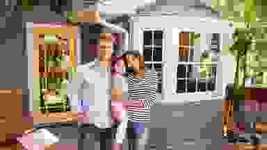 一对夫妇与一个小孩站在一个房子前面有移动的箱子