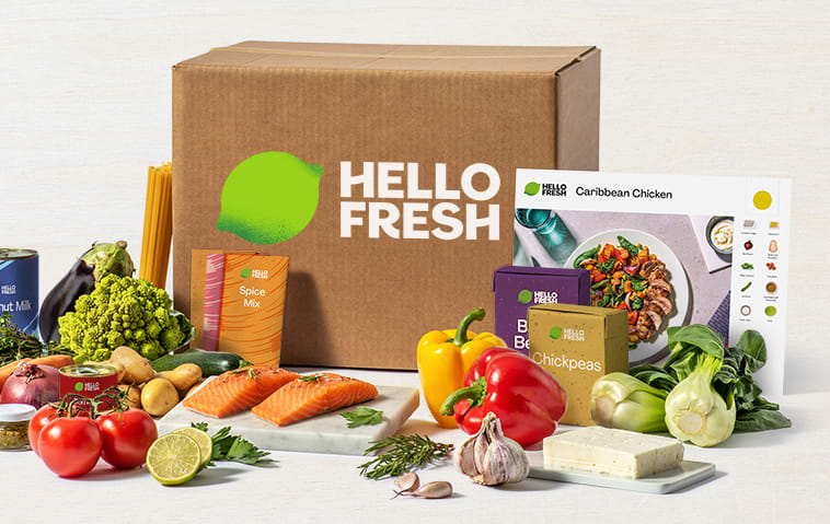 A HelloFresh box and recipe book next to various ingredients and vegetables.