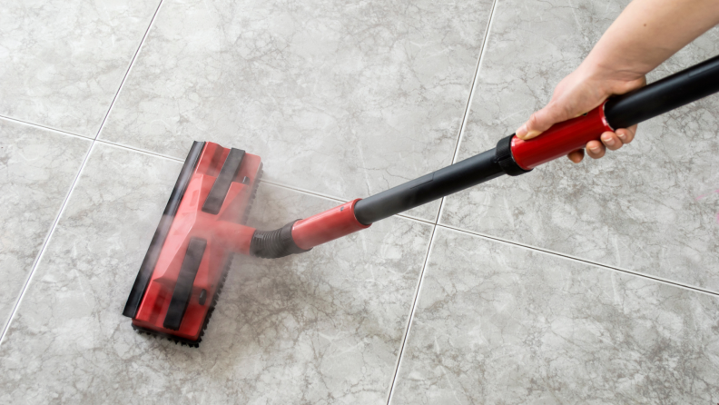 A person cleans a floor with a steamer.