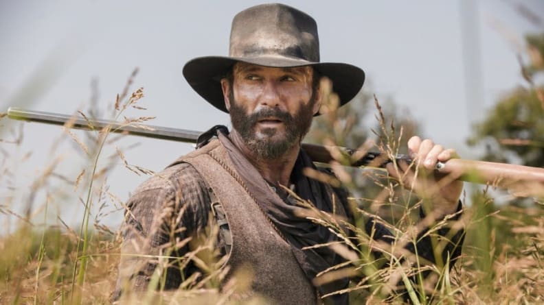 A cowboy stands in the middle of an open plain.