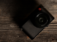 A black Leica Q (Typ 116) camera sits on a wooden table facing up