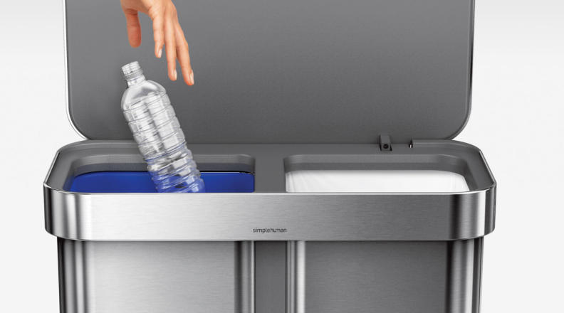 A plastic water bottle is tossed into the recycling side of the Simplehuman dual trash can.