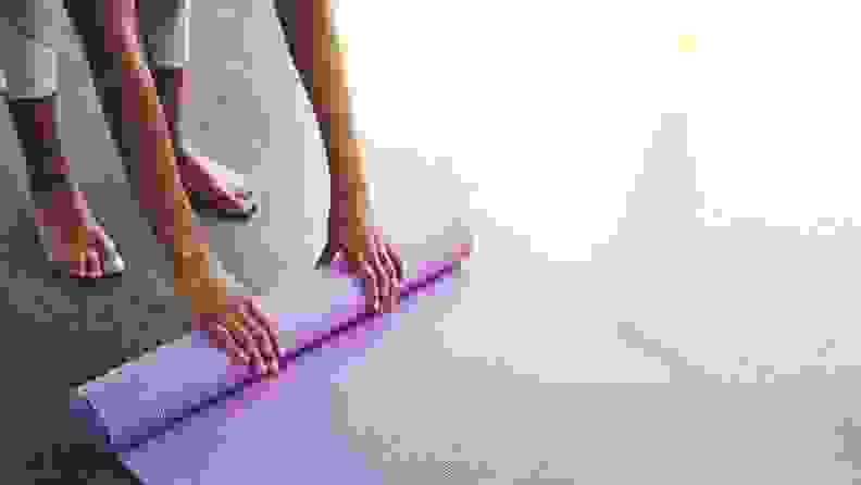 A person unrolls a yoga mat on a hard wooden surface.
