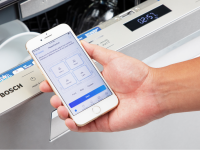 A Bosch dishwasher and a hand holding a smartphone displaying the Bosch app.