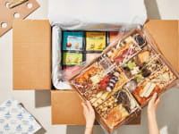 CheeseBoarder cheese board wrapped in plastic, being pulled from its cardboard box.