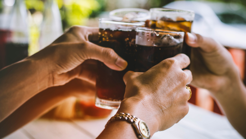 A group of people clink glasses full of soft drinks.