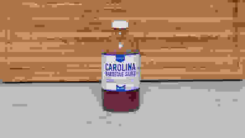 A bottle of Lillie’s Q Carolina Barbeque sauce next to a wood cutting board.