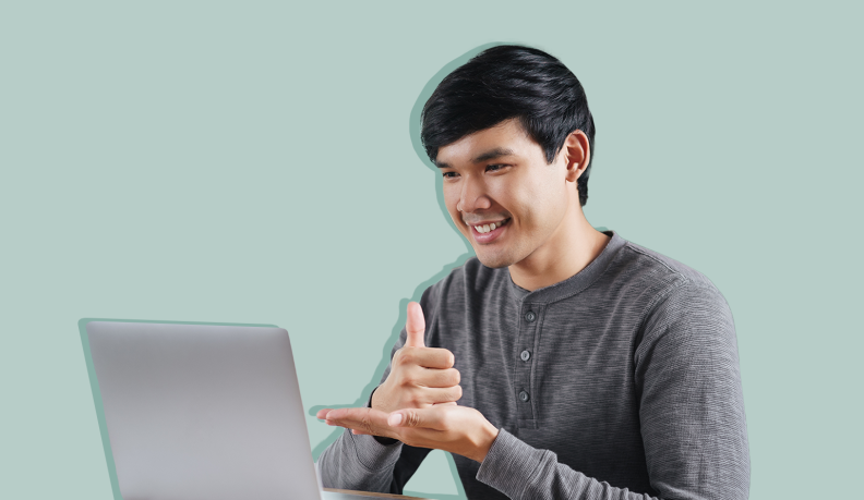 Person smiling while working at computer while using ASL to communicate.