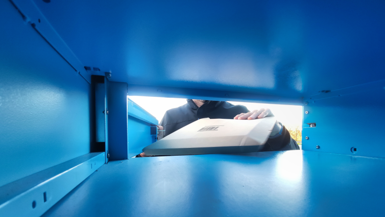 A person places a package inside a blue mailbox