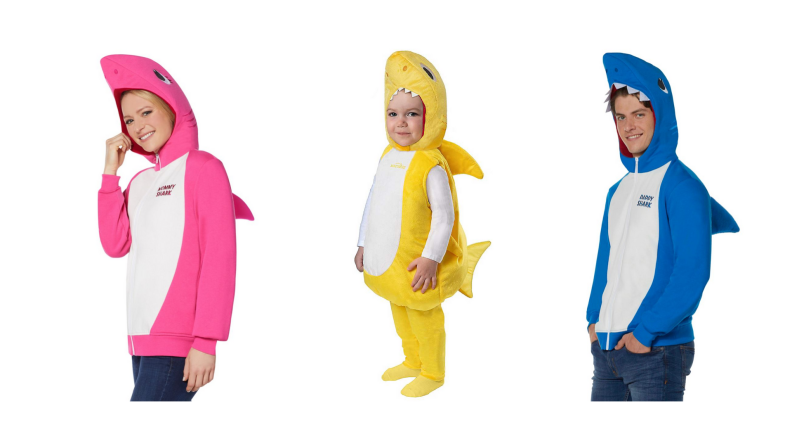 A family in Baby Shark costumes: A woman in a pink shark, a baby in a yellow shark, a man in a blue shark.