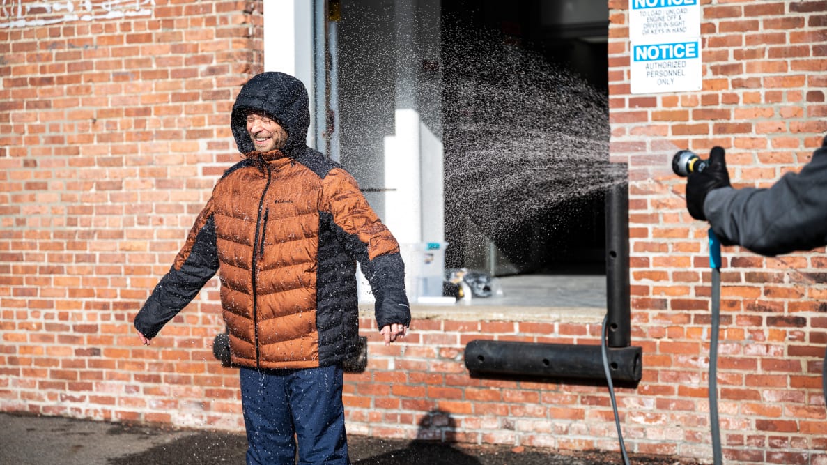 Man sprayed with a water hose while wearing a Columbia Omni-Heat Infinity Padded Hooded Jacket.