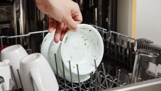 A person pulling out a dirty white bowl from a dishwasher top rack