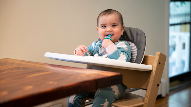 A child sitting in the Stokke Tripp Trapp high chair chewing on a spoon.