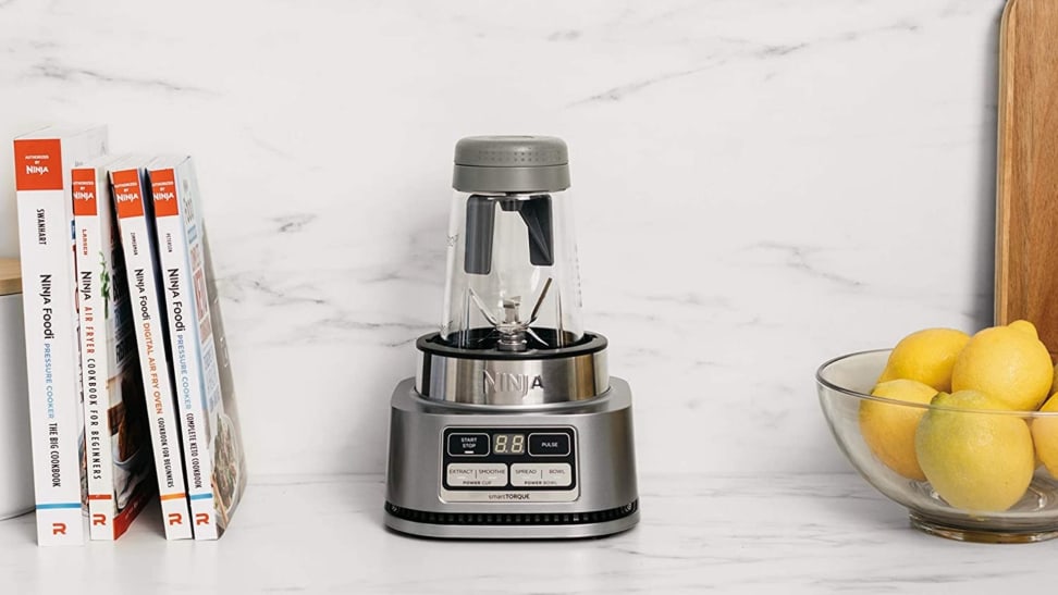 A closeup of a Ninja Foodi Smoothie Bowl Maker and Nutrient Extractor on a countertop surrounded by cookbooks and a bowl of lemons.