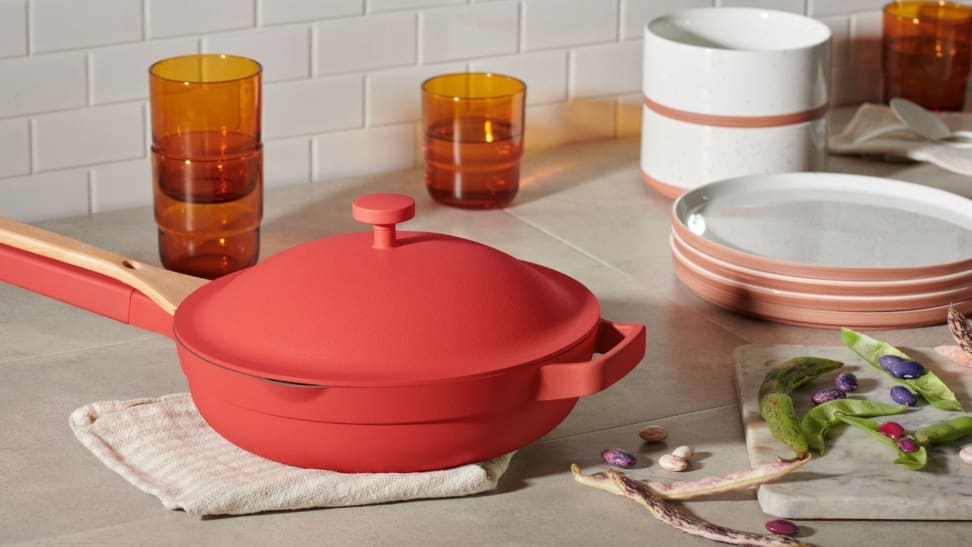 A red pan sits on a kitchen counter surrounded by other serving pieces.