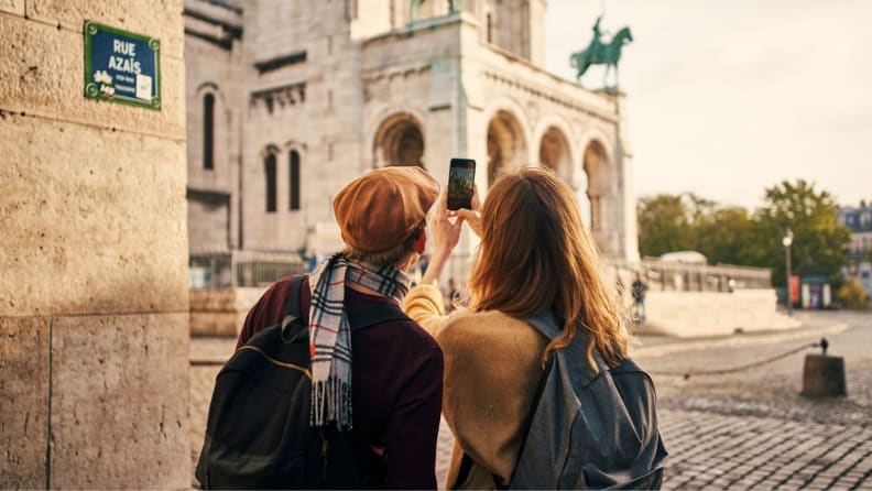 A pair of tourists wearing backpacks take a photograph of a building in Paris