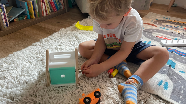 A little boy sits on the floor and plays with toys.