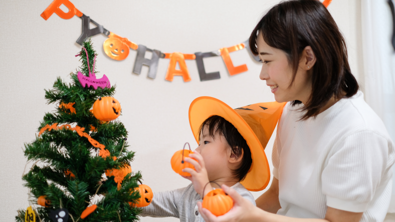 A woman and a child happily decorate a Halloween tree.