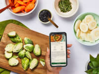 A countertop with healthy ingredients chopped, with a hand holding a phone that showcases a recipe